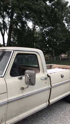 an old white pickup truck parked on the side of the road with trees in the background