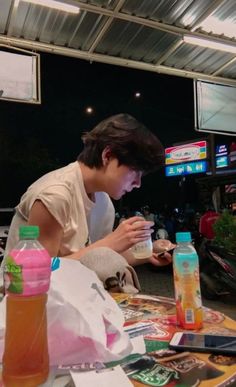 a young man sitting at a table with drinks in front of him and looking at his cell phone