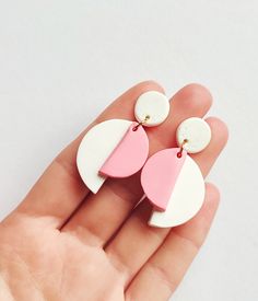 a hand holding two white and pink earrings