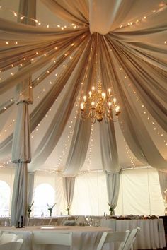 the inside of a tent with white curtains and chandelier hanging from it's ceiling