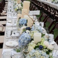 a long table is set with white and blue flowers, candles, and place settings