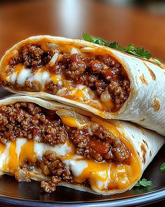 two burritos sitting on top of a plate covered in cheese and chili sauce