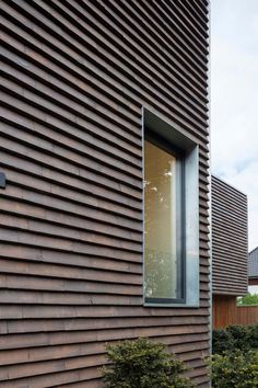 the side of a wooden building with a window on it's side and bushes in front