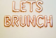 balloons spelling the word let's brunch on a white wall with gold foil letters