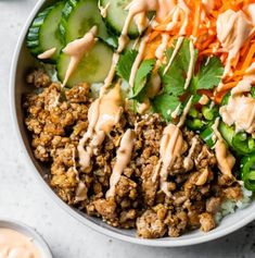 a white bowl filled with meat and veggies on top of rice next to dipping sauce