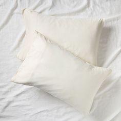 two white pillows sitting on top of a bed next to an unmade pillow case