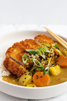 pork curry with vegetables and rice in a white bowl next to chopsticks on the side