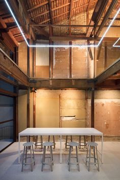 an empty room with tables and stools in the center, surrounded by wooden beams