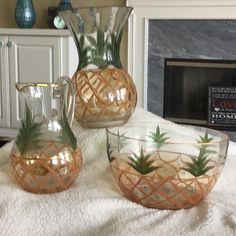 three glass vases with plants in them sitting on a white blanket next to a fireplace