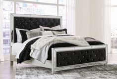 a white bed with black and silver decor on it's headboard, in front of a window