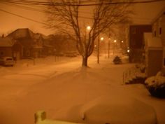 a snow covered street at night with cars parked on the side and houses in the background