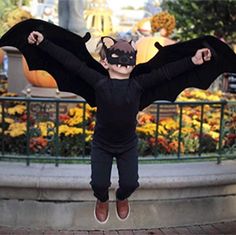 a young boy wearing a bat costume jumping in the air with his arms spread wide