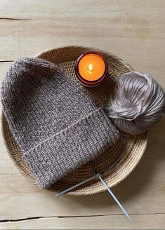 a gray knitted hat sitting on top of a wooden table next to a candle