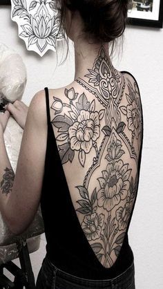 a woman with tattoos on her back holding a teddy bear and looking at the wall