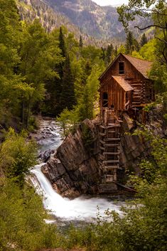 an old wooden building sitting on top of a cliff next to a river and waterfall