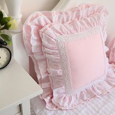 a pink pillow sitting on top of a bed next to a white nightstand with a clock