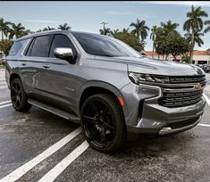 a silver chevrolet suv is parked in a parking lot with palm trees and buildings behind it