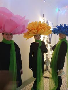 three people wearing hats and scarves in front of a mirror with flowers on their heads