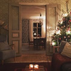 a living room filled with furniture and christmas trees in the corner, lit up by candles