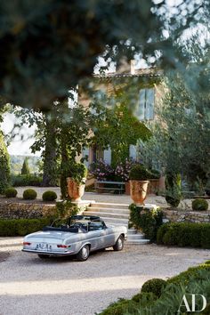 a car is parked in front of a house with trees and bushes around the driveway