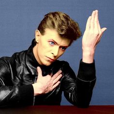 a man in black leather jacket sitting at a table with his hand on his chest