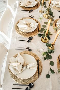 the table is set with black and white plates, napkins, candles and greenery