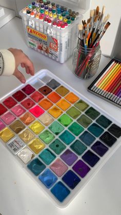 a person is painting with watercolors on a white surface next to other supplies