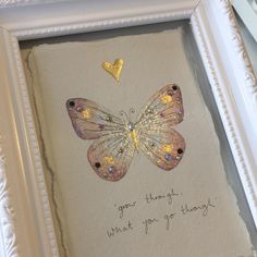 a white frame with a yellow butterfly and some writing on the inside, in front of it is a gold heart