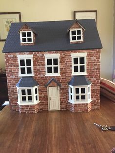 a toy brick house with windows and doors on a wooden table next to a pair of scissors