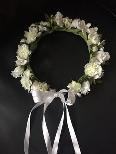 a wreath with white flowers and ribbons on a black surface, tied in a bow