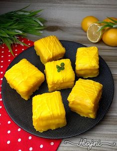 several pieces of yellow cake on a black plate next to oranges and green leaves