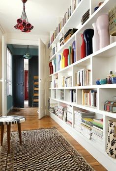 a living room filled with lots of books on white shelving units next to a table