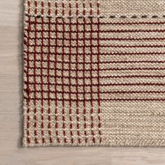 an area rug with red and white checkered squares on the side, in front of a wooden floor