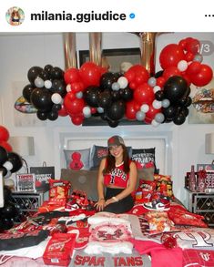 a woman sitting on top of a bed covered in red, white and black balloons