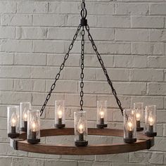 a chandelier with candles in glass jars on a wooden ring hanging from a brick wall