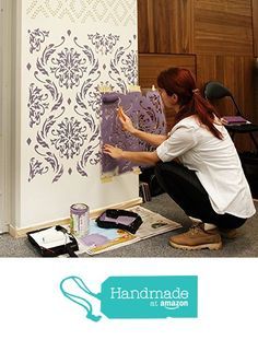 a woman is painting a wall with purple stencils