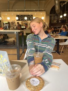 a woman sitting at a table with a cookie and drink