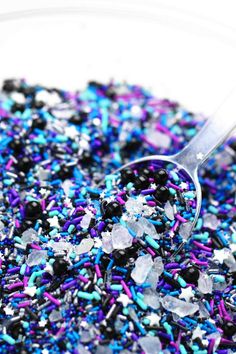 sprinkles in a glass bowl with a spoon on the side and blue, purple, and white sprinkles