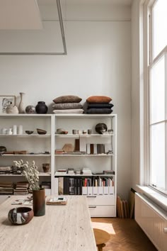 a room with several shelves filled with books and vases on top of them next to a window