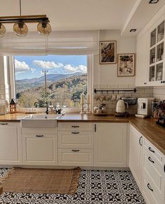 a kitchen with white cabinets and black and white tile flooring next to a window