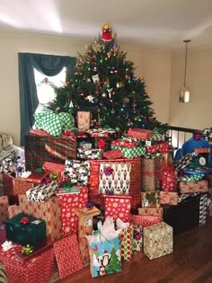 a christmas tree with presents under it in front of a pile of wrapped presents on the floor