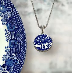 a blue and white plate sitting next to a necklace that has a design on it