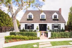 a white house with black shutters on the front and side windows, surrounded by greenery