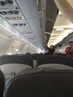 the inside of an airplane with people sitting and standing on it's seats,