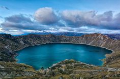 a blue lake surrounded by mountains under a cloudy sky