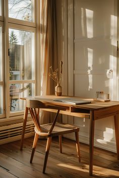 a wooden desk sitting in front of a window next to a vase with flowers on it