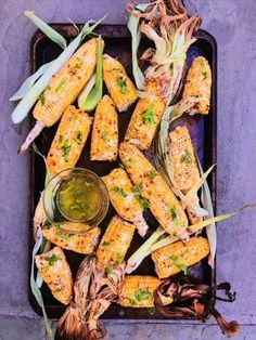 grilled corn on the cob with butter and parsley next to a bowl of dipping sauce