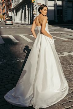 a woman in a white dress is standing on the street and looking at something behind her