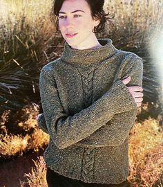 a woman standing in the desert with her arms crossed and wearing a sweater over her shoulders