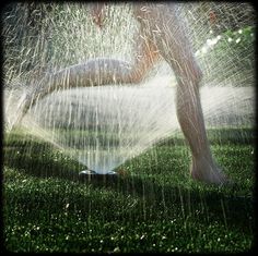 a person standing under a sprinkle in the grass with their legs spread out